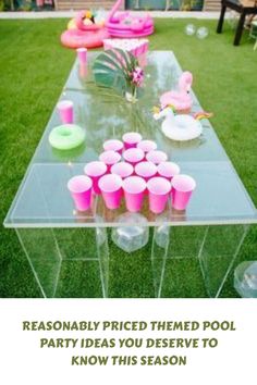 a clear table with pink cups and flamingos on it in front of a lawn