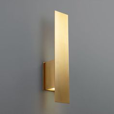 a wall mounted light on the side of a gray wall with a gold colored finish