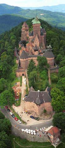 an aerial view of a castle in the middle of trees and mountains with cars parked around it