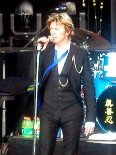 a man in a tuxedo singing into a microphone on stage with other instruments behind him