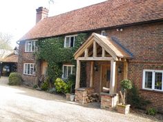 a brick house with an attached porch and covered in ivy on the outside wall, next to a gravel driveway