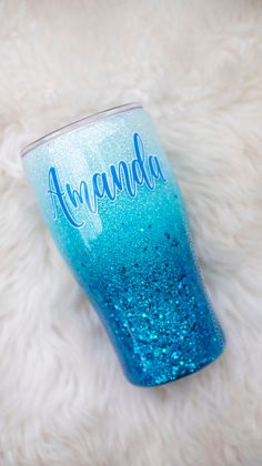 a blue and green glittered cup sitting on top of a white fur covered floor