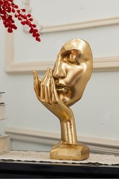 a golden statue is on a table next to some books and a vase with red flowers