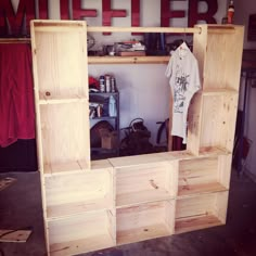 an unfinished wooden shelf with clothes hanging on the top and shelves below it that are made out of plywood