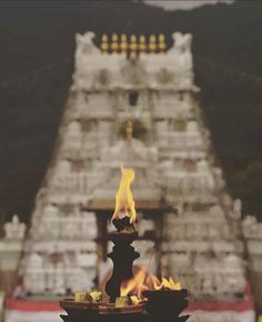 a fire burning in front of a very tall structure with many pillars and lights on it