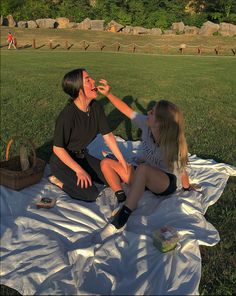 two people are sitting on a blanket in the grass and one person is reaching for something