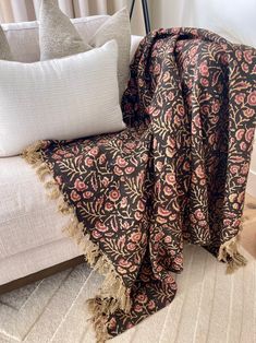 a black and pink blanket sitting on top of a white couch next to two pillows