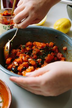 two hands holding a spoon over a bowl of food