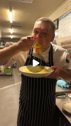 a man in an apron is eating spaghetti from a white plate and holding a fork