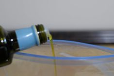 a bottle of olive oil is being poured into a plastic container with a blue lid