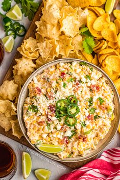 a bowl of mexican dip surrounded by tortilla chips, limes and jalapenos