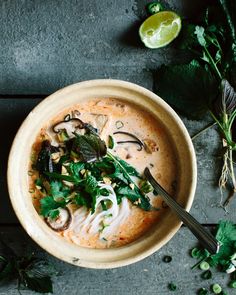 a bowl filled with soup and garnished with cilantro, parsley and lime