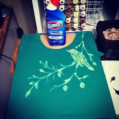 a green t - shirt with a bird on it next to a bottle of clorol