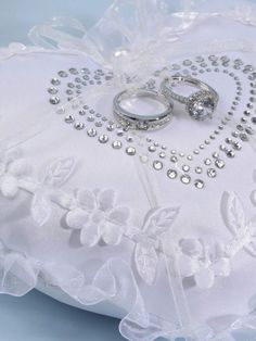 two wedding rings sitting on top of a white pillow with beaded trimmings