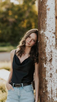 a beautiful young woman leaning against a wooden pole