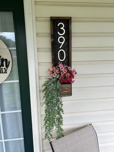 a wooden sign hanging on the side of a house next to a chair and flower pot