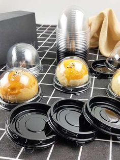 six black plates with silver lids on a gray table cloth next to some napkins