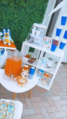 a table with cupcakes, cookies and drinks on it in front of a hedge