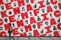 a man walking past a large red and white wall covered in letters, numbers, and symbols