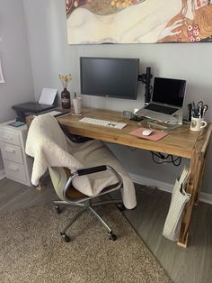 a desk with a computer, laptop and chair in front of a painting on the wall