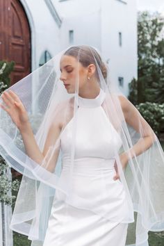 a woman wearing a white wedding dress and veil in front of a church door with her hands on her hips