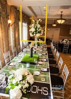 a long table set up for a football themed event with flowers and place settings on it