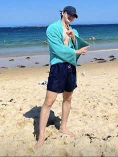 a man standing on top of a sandy beach next to the ocean with his hands in his pockets