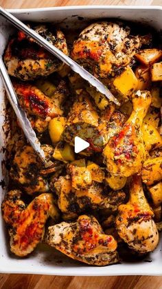 a pan filled with chicken and potatoes on top of a wooden table next to a knife