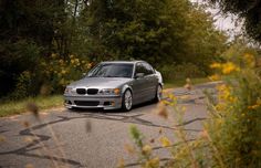 a silver car parked on the side of a road in front of trees and bushes