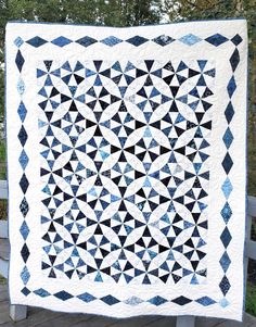 a black and white quilt on a wooden bench with trees in the backround