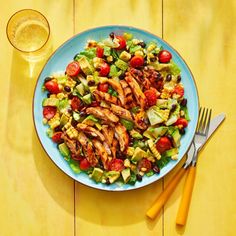 a blue plate topped with chicken and salad next to a glass of orange juice on top of a yellow table