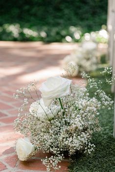 white roses and baby's breath are arranged in a vase on the brick walkway