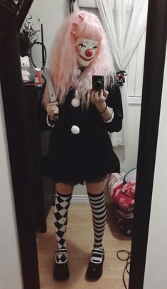 a woman with pink hair and clown makeup is taking a selfie in the mirror