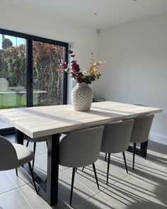 a vase with flowers sitting on top of a wooden table next to some gray chairs