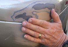 an older person's hand on the bumper of a car that has been painted with gray paint