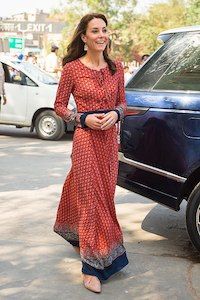 a woman in a red dress is standing next to a blue car and smiling at the camera