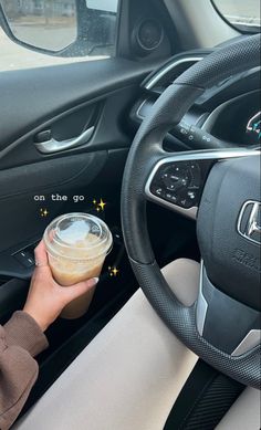 a person holding a cup in their hand while driving the car with steering wheel controls