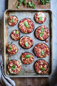 an overhead view of several baked pizzas on a baking sheet, with basil leaves