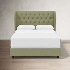 a bed with white pillows and green headboard in a room that has hardwood floors