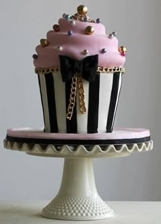 a pink and black cupcake decorated with jewels on a white cake stand in front of a gray wall