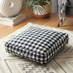 a black and white checkered pillow sitting on top of a rug next to a plant