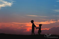 two children are holding hands as the sun sets in the sky behind them, silhouetted against an orange and blue sunset