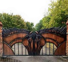 an iron gate with two horses on it in the middle of a driveway surrounded by trees