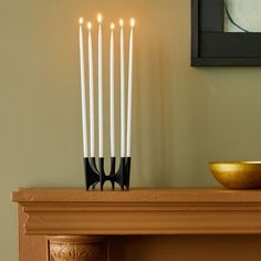 five candles are lit on a mantle with a bowl in the corner next to it