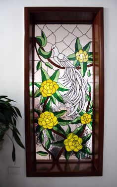 a stained glass window with yellow flowers and leaves on the bottom half, in front of a potted plant