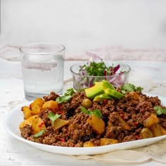 a white plate topped with meat and veggies next to a glass of water