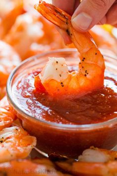 someone dipping shrimp into a small bowl of marinara sauce on top of other foods