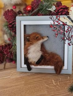 a stuffed fox in a frame on a table with pine cones and other holiday decorations