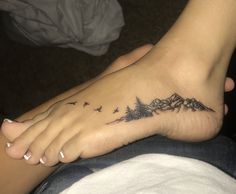 a person has a tattoo on their foot with mountains and birds flying above them in the air