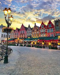 the sun is setting in front of many buildings and bicycles are parked on the street